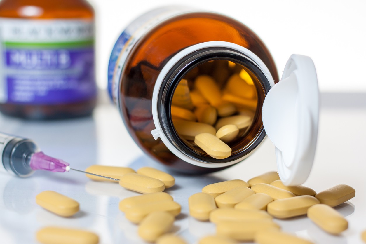 Opioid pills spilling out of medicine bottle with syringe next to it