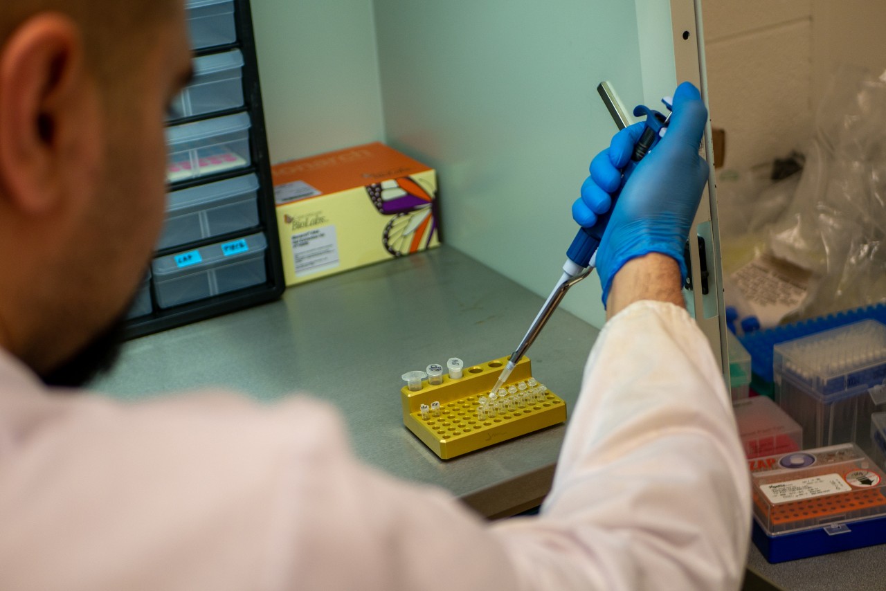 Asshish Priye puts a sample into a vial on a lab bench with one gloved hand.