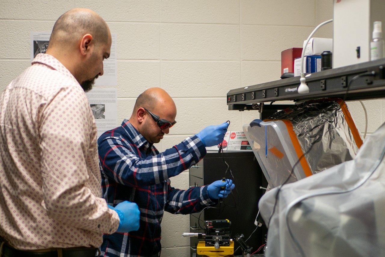 Priye and grad student in lab work with lab equipment.