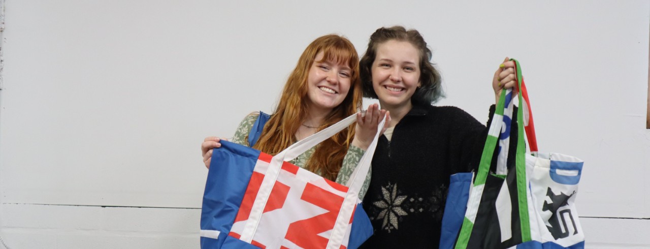 UC student volunteersCaroline Bussick and Hannah Weisburn holding tote bags.