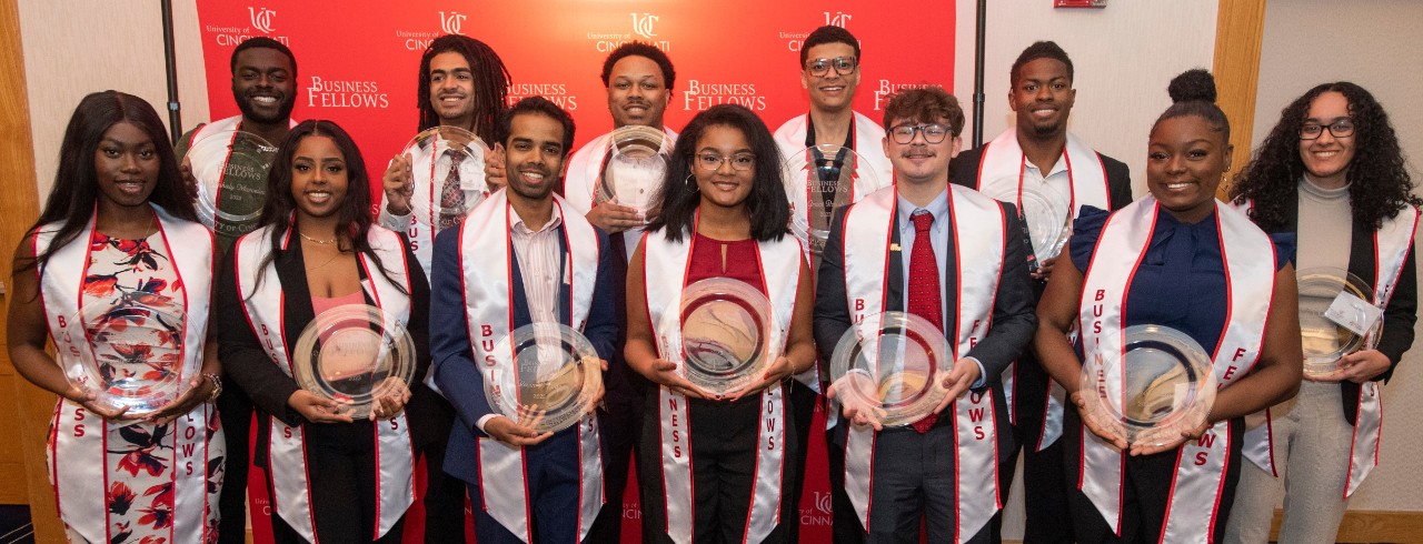12  graduates of Lindner Business Fellows pose wearing graduation stoles and holding commemorative plates