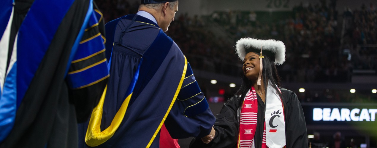 A smiling student shakes hands with Provost Valeria Ferme on stage at Fifth Third Arena.