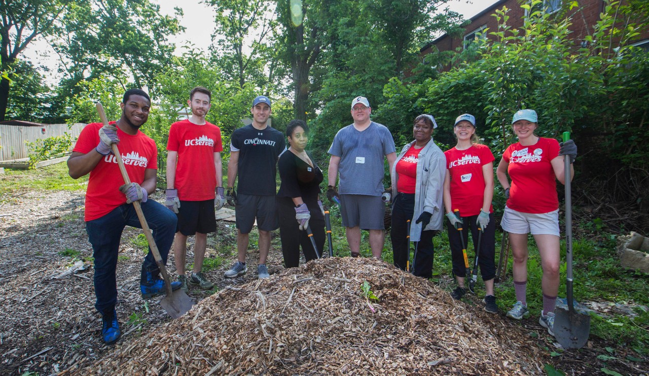 A group of staff and faculty pose with shovels with a pile of mulch at their UC Serves site