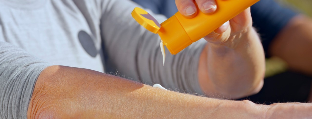 A person squeezes sunscreen from a bottle onto their arm