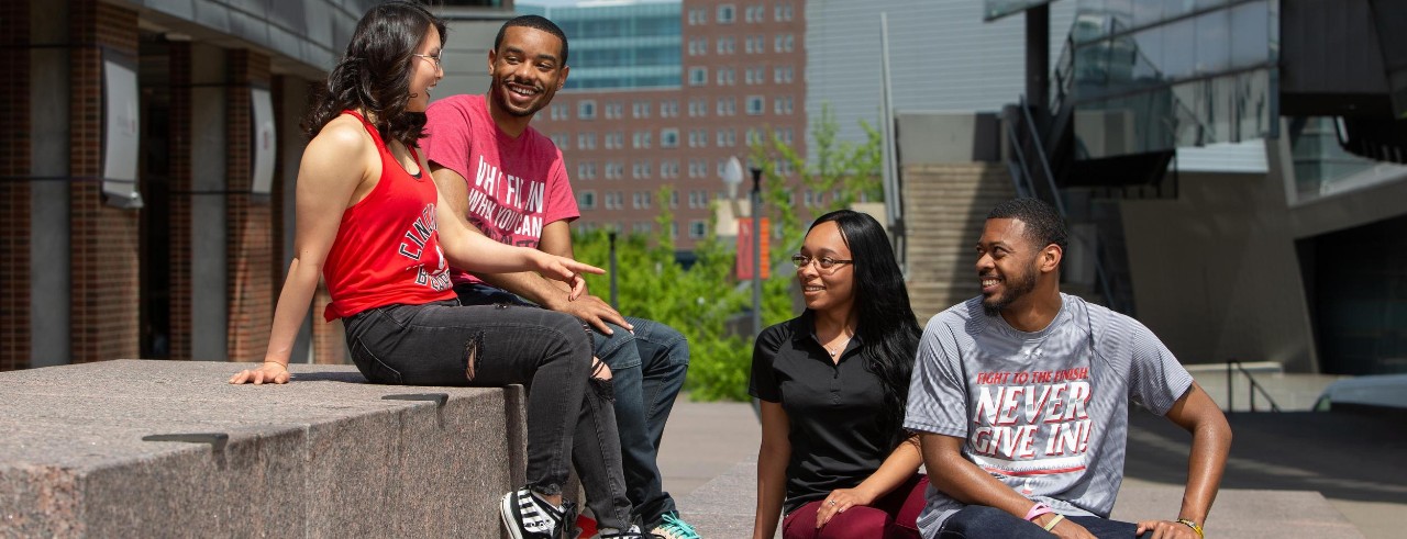 Four University of Cincinnati students sitting together and talking on main campus
