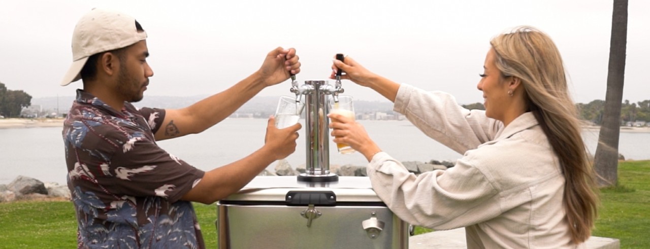 A man and a woman pour drinks from the Cooler Keg at a lake.