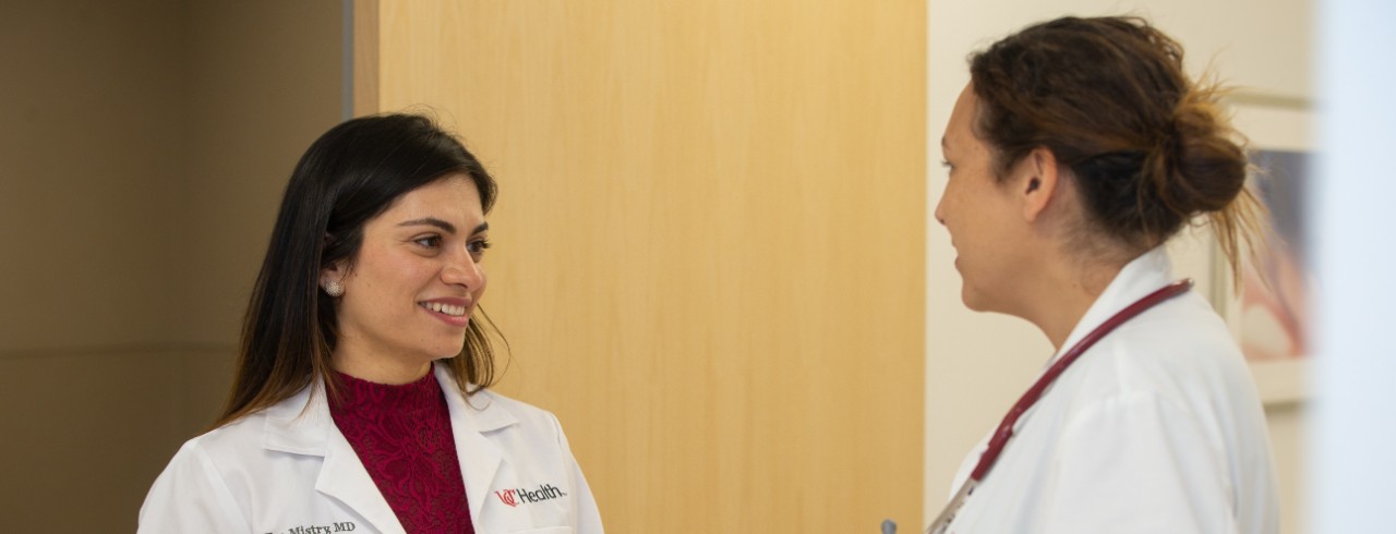 Two doctors wearing lab coats talk to each other