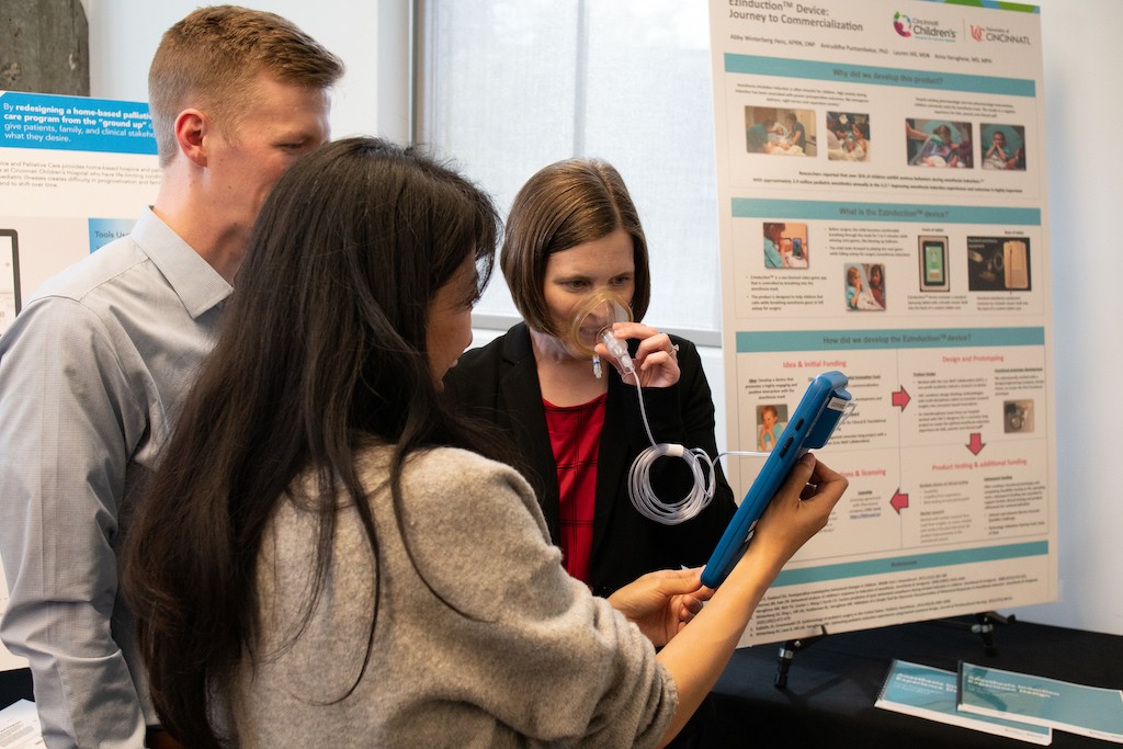 Woman with anesthesia mask looks at laptop held by other woman while man observes