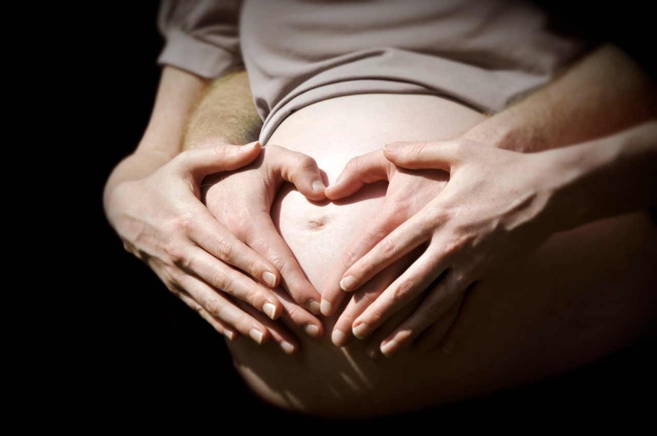 a photo of a man and a woman with their hands illuminated on a pregnant women's belly