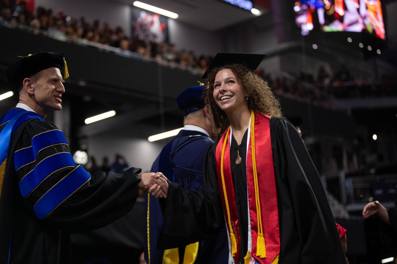 Students shakes hand of faculty member on commencement stage