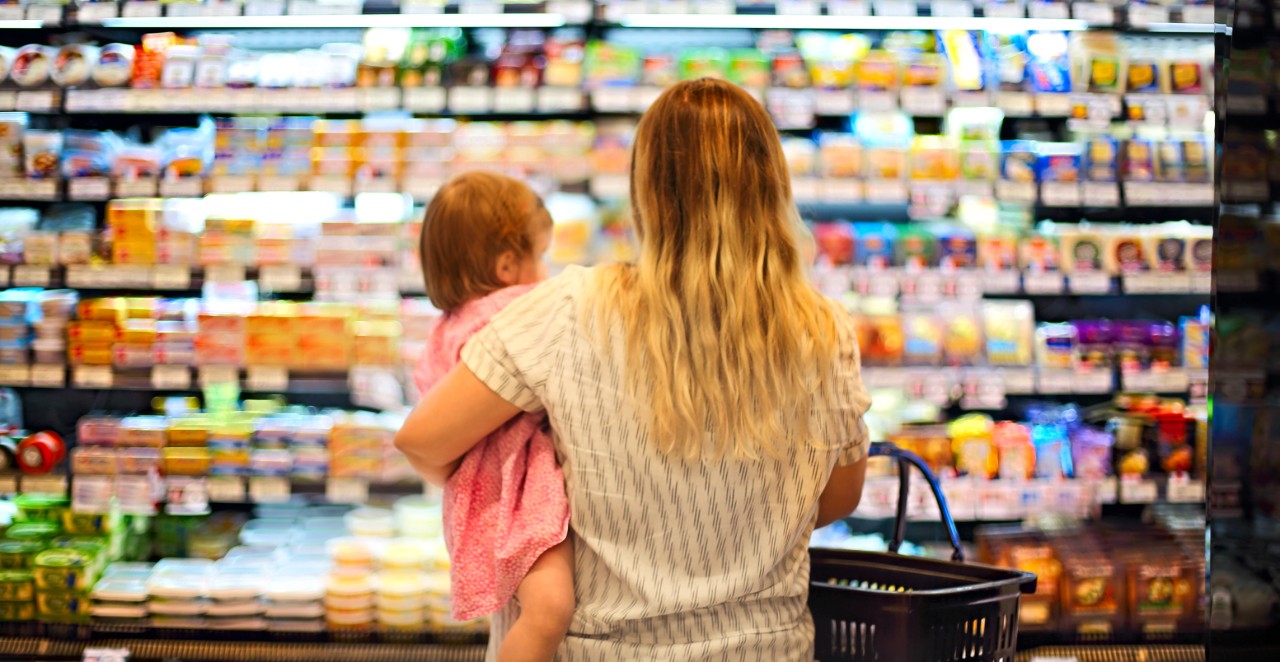 rear view of woman holding a baby in a grocery store looking at options on the dairy aisle