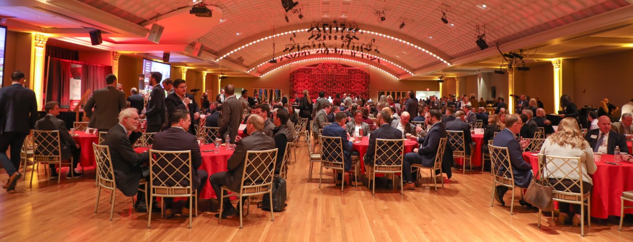 A crowd of people at a real estate event sit at round tables.
