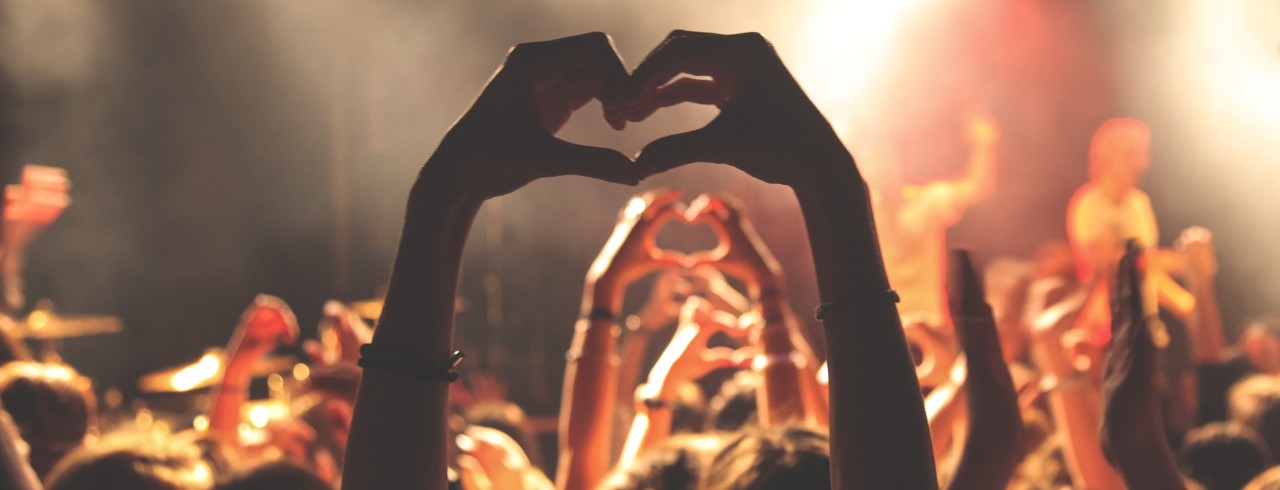 Attendees at a concert make hearts with their hands and fingers