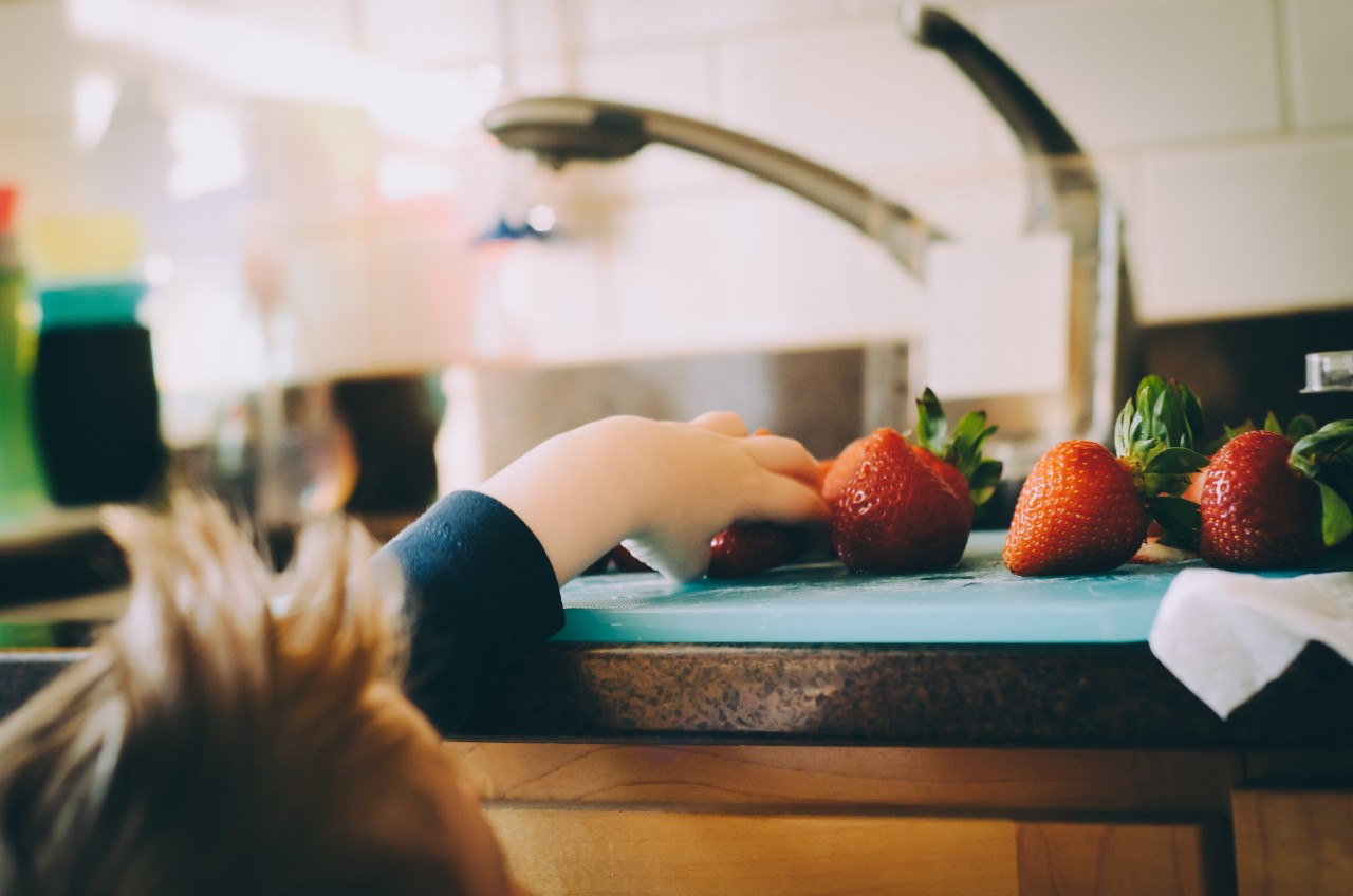 small child reaching up to the counter to get a strawberry 