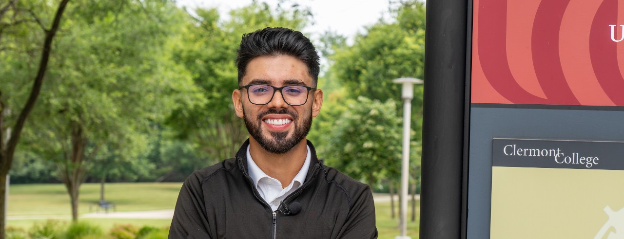 Student Spencer Singh smiling by the UC Clermont campus sign and map