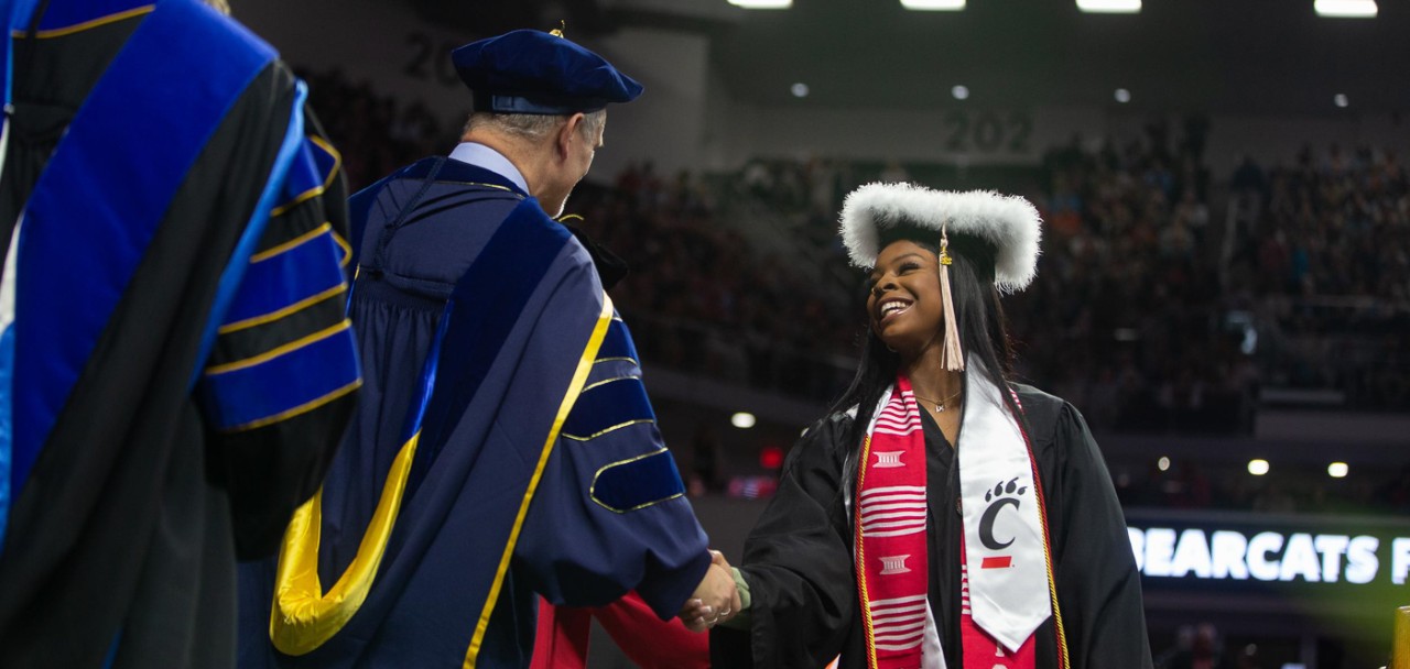 A UC graduate accepts congratulations on stage at Fifth Third Arena.