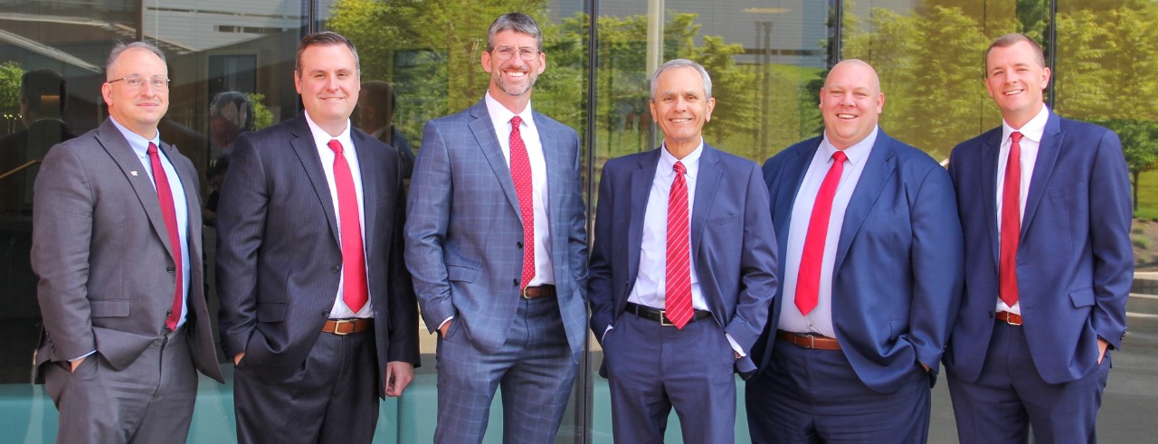 1819 Wealth Advisors, dressed in dark suits and red ties, stand outside of Lindner Hall.
