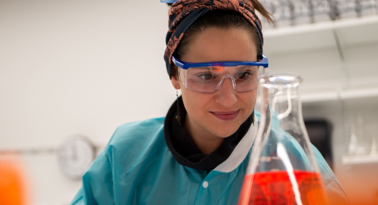 A researcher in a labcoat studies a beaker of fluid in a Bioscience Center lab.