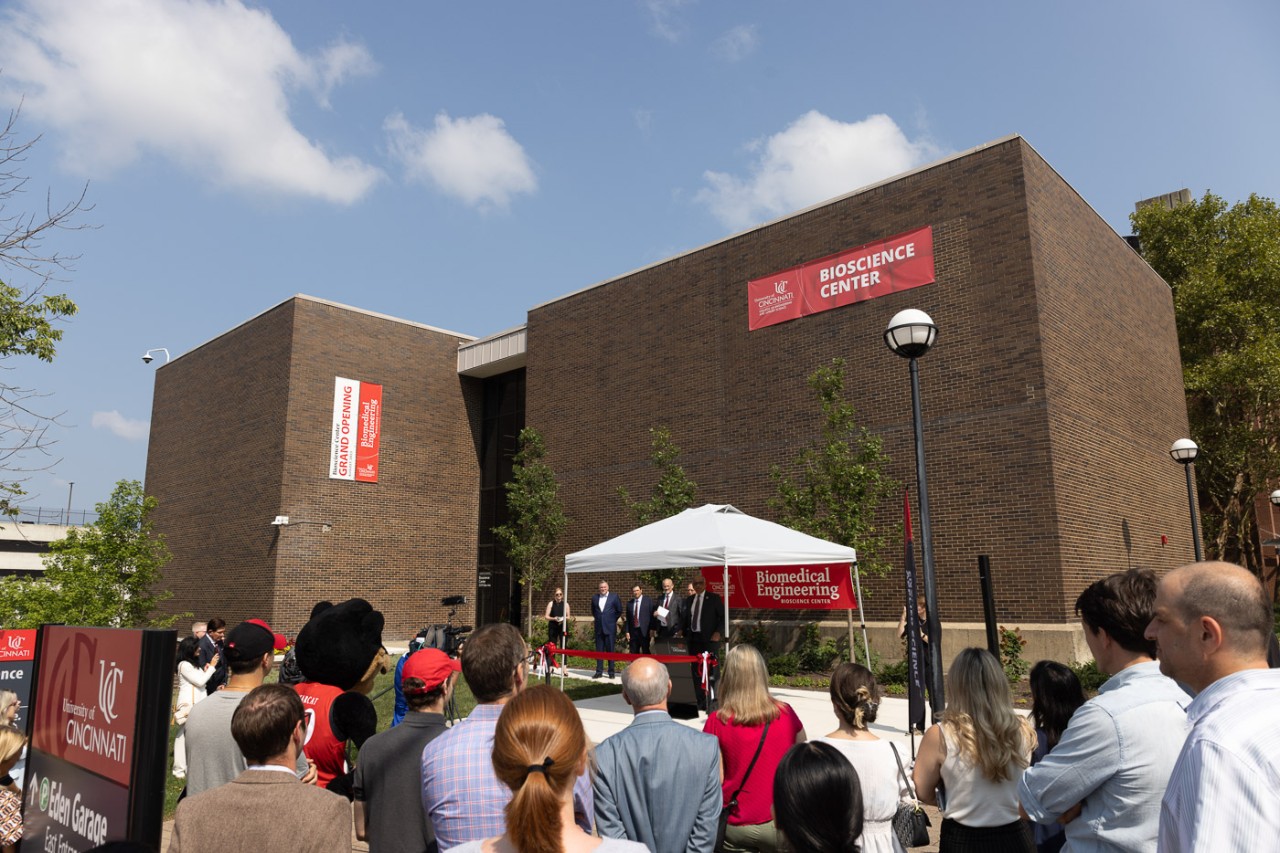 A group of people listen to speakers under a tent in front of the Bioscience Center.