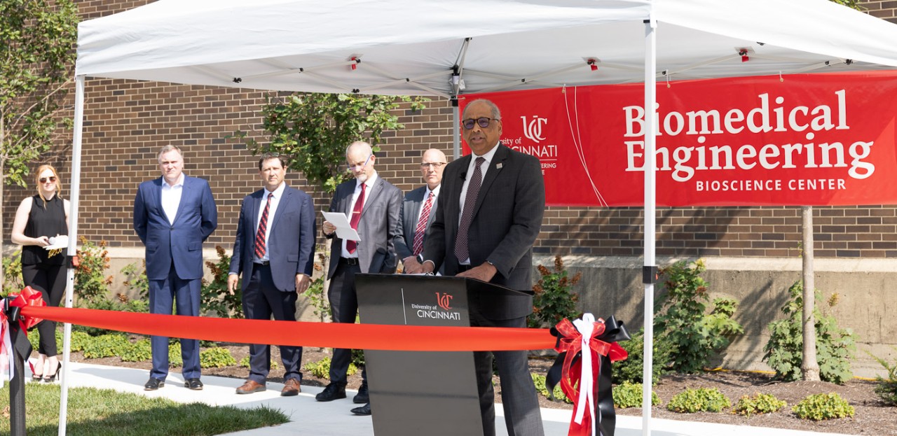 UC President Neville Pinto stands at a podium in front of a Biomedical Engineering banner.