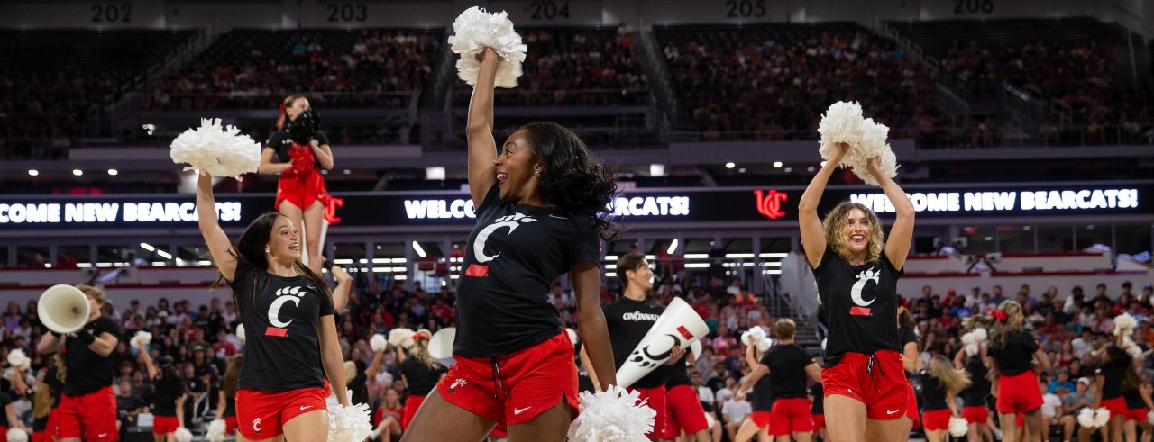Image of the UC Cheer Team at Fifth Third Arena with a Welcome New Bearcats sign nearby