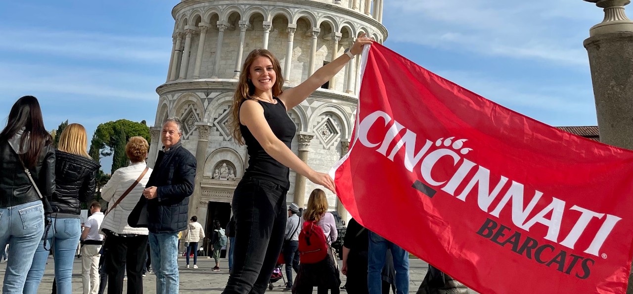 Student holding UC flag in front of the Leaning Tower of Pisa