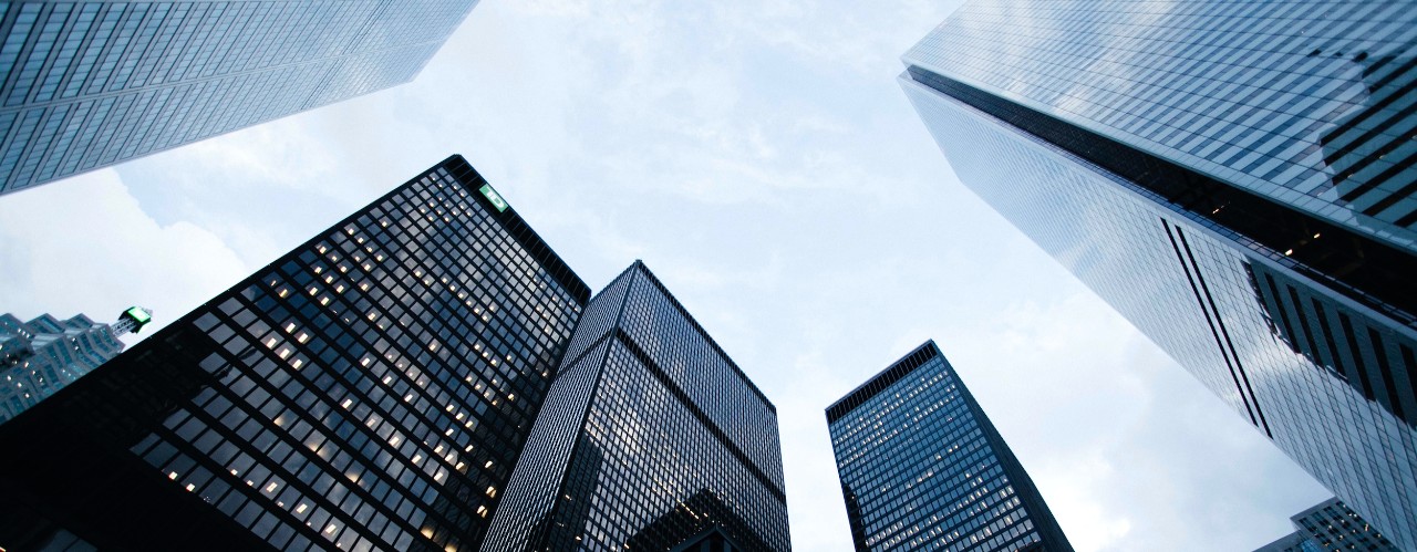 Skyward view of four skyscraper buildings under blue skies.