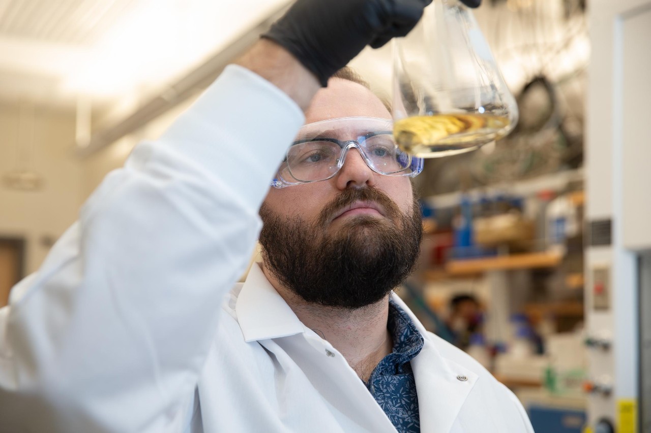 A chemist in a UC lab holds up a beaker of fluid.