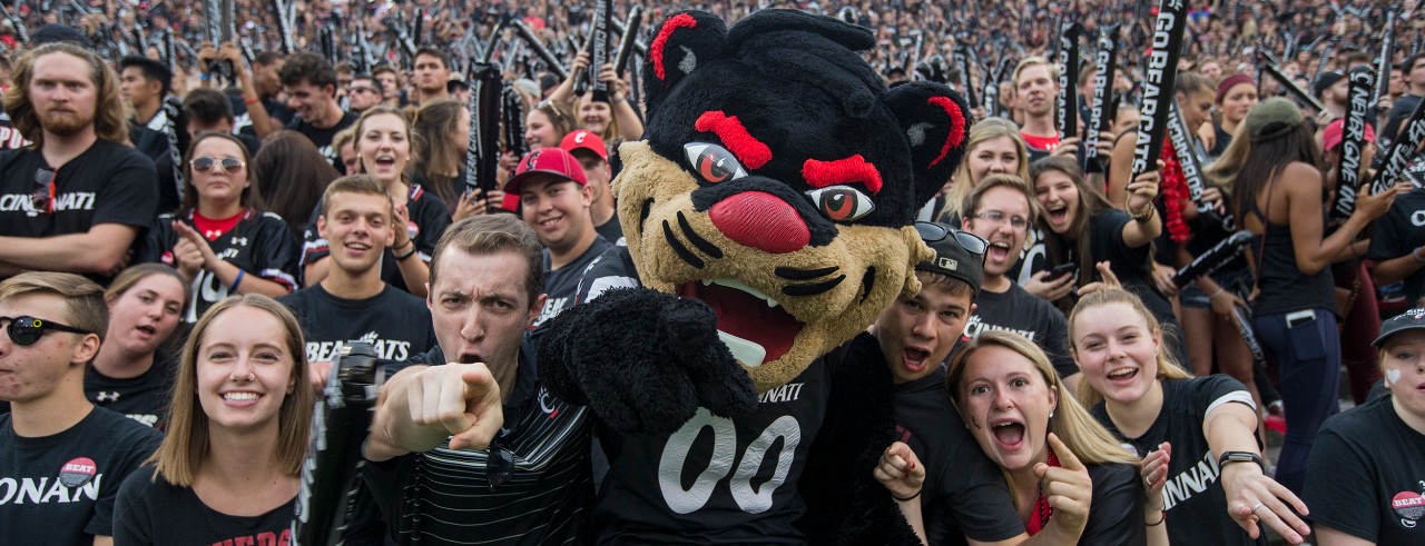 UC bearcat celebrates with students at a football game.