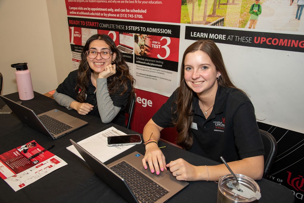 Two student workers sit at a table during an open house event