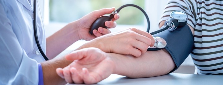 A health professional takes a person's blood pressure on their right arm using a blood pressure cuff