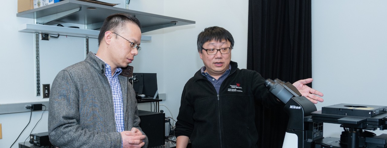 Sun and Diao talk in the lab in front of a microscope
