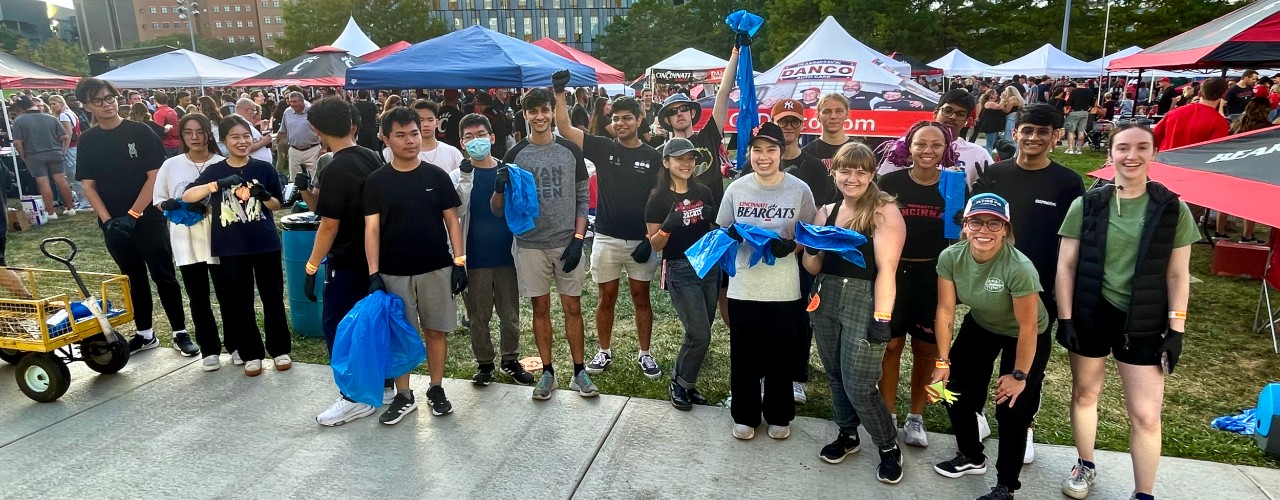 UC Sustainability volunteers standing together in Sigma Sigma Commons holding blue bags of recyclable cans and bottles.