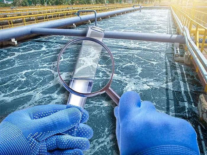 a graphic of two hands in medical gloves examining a water sample with a magnifying glass