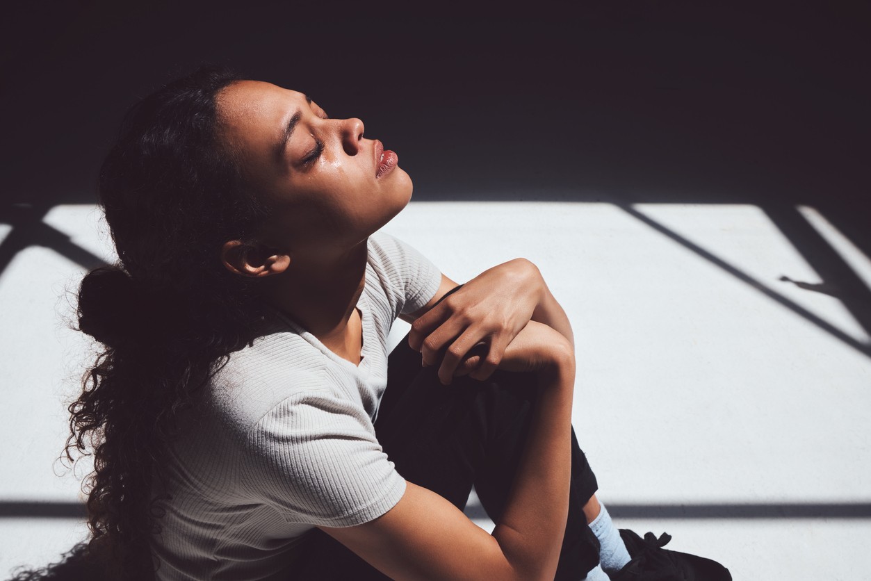 Young woman sitting on floor, cryting with face uplifted