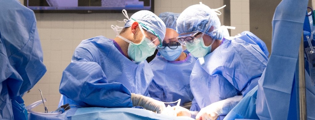 Three surgeons wearing masks and gowns work on a patient in the operating room