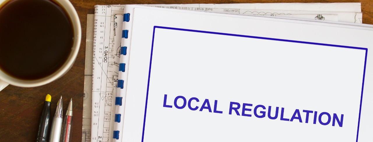 A booklet on a table with pens and a cup of coffee to the left with the words 'Local Regulation' printed on it.