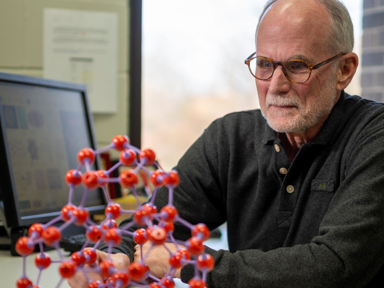 Clifford Larrabee, retired UC Clermont chemistry professor and researcher, who has received a patent for his novel cancer drug delivery system, looks at a research model in his office.