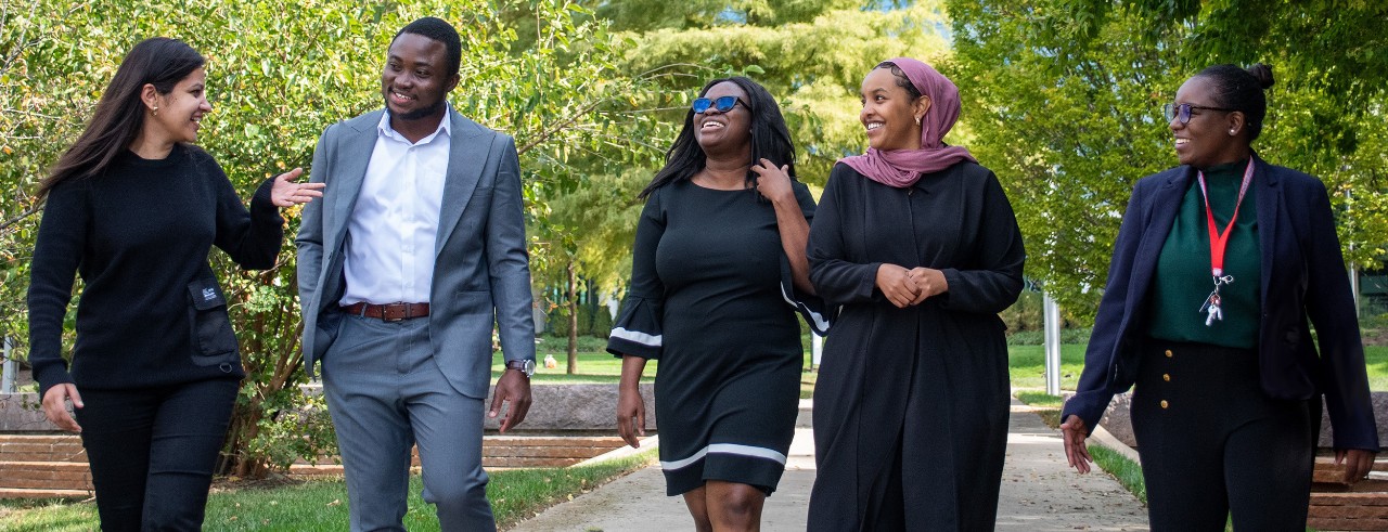 Five people walk along a pathway at UC, chatting and smiling