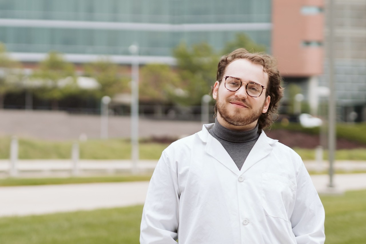 Trenton Stern dressed in white medical coat shown outside with the College of Medicine in the background