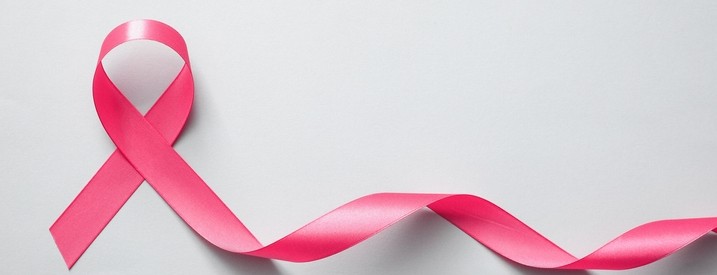 An upturned horseshoe painted pink with pink and white polka dot ribbon and  a heart shaped slate shape on a white table with pink background. Breast  cancer awareness message Stock Photo