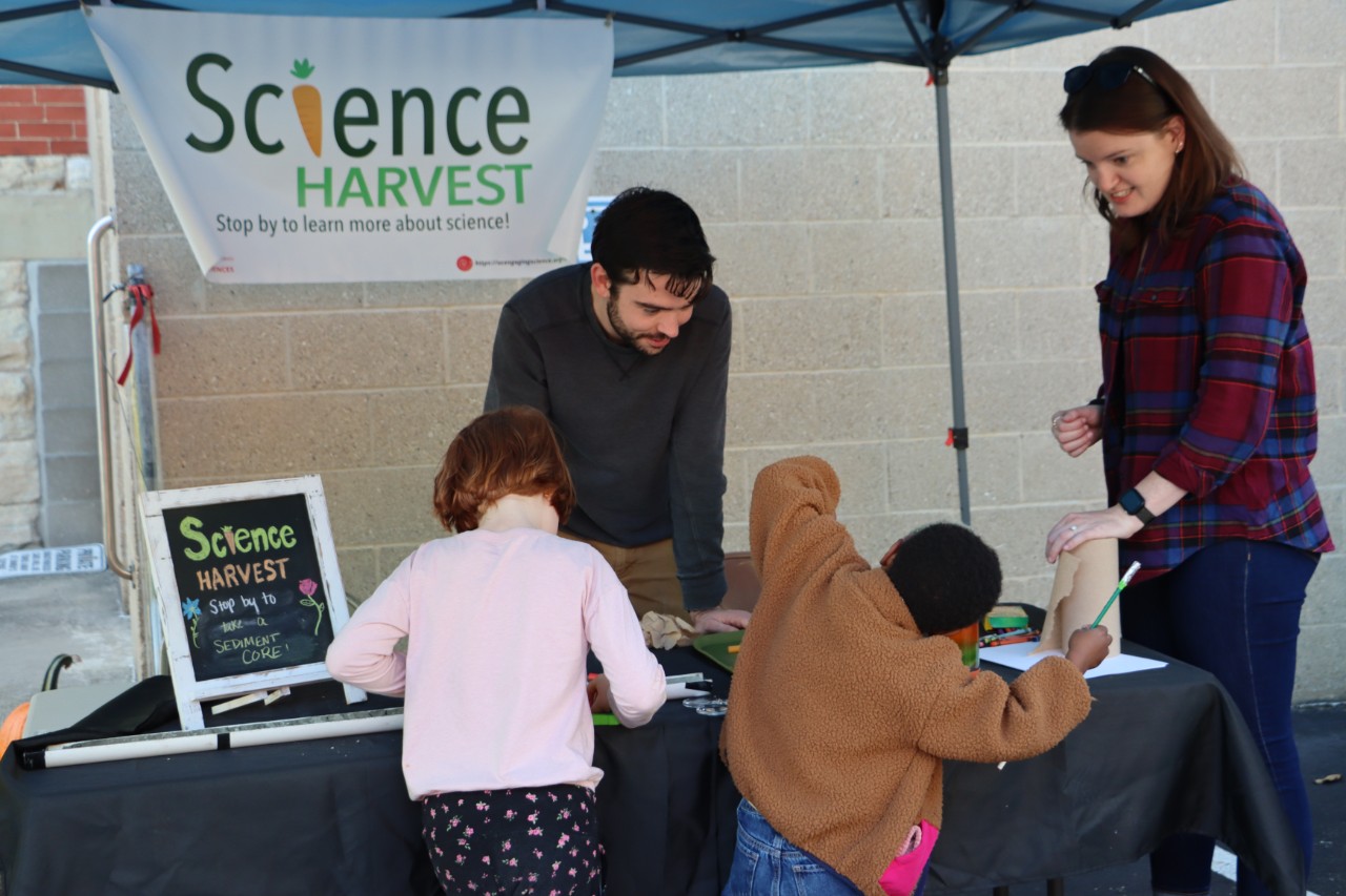 Science Harvest tent with two young kids and a parent standing in front. 