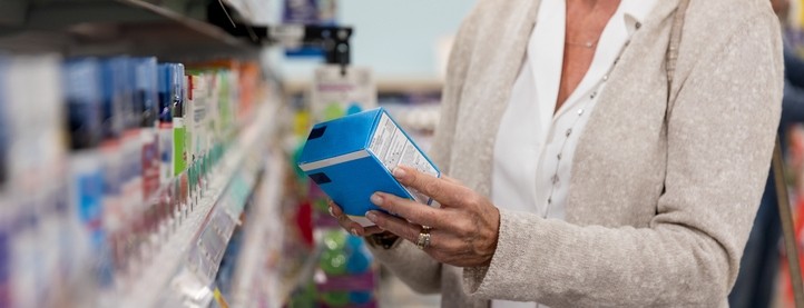 A woman holds an over the counter medicine in her hands in an aisle of a pharmacy