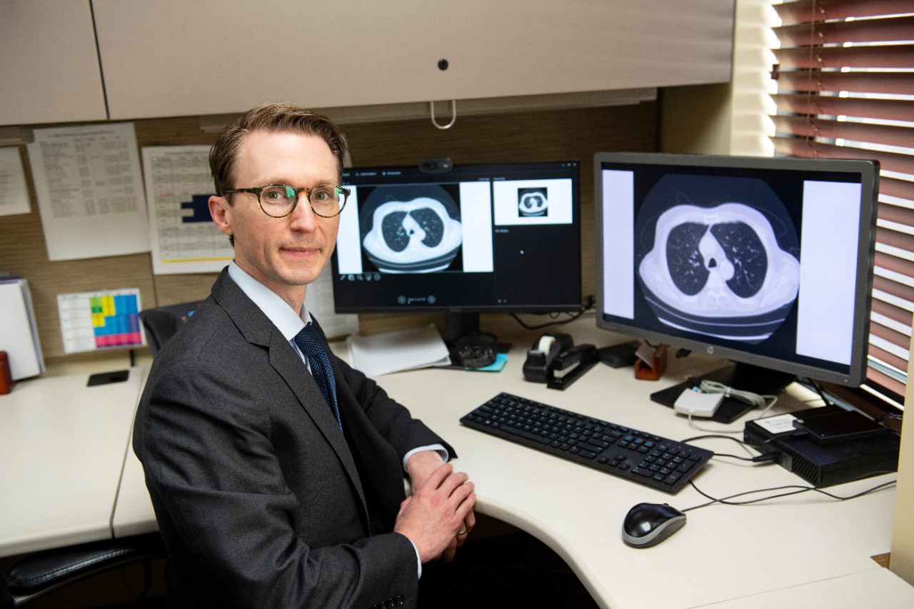 Robert Van Haren sits at his desk with an image of a lung scan on a computer monitor behind him