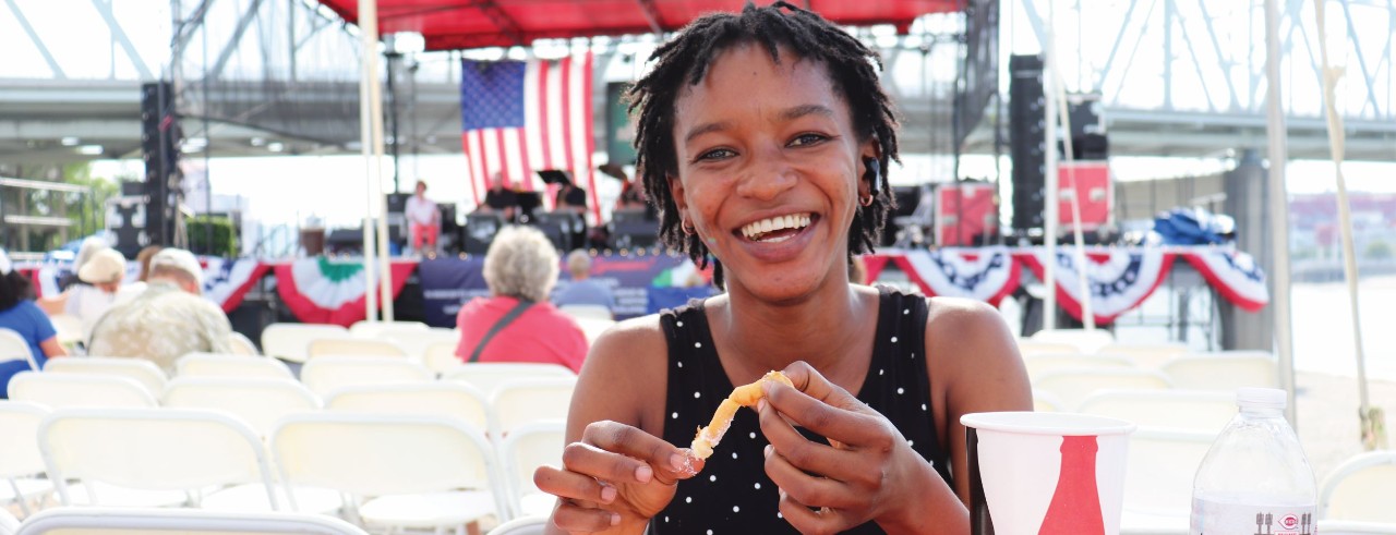 UC Information Systems graduate Aissatou Barry smiles at the camera and eats a snack at the Italian Fest in Newport, Kentucky.