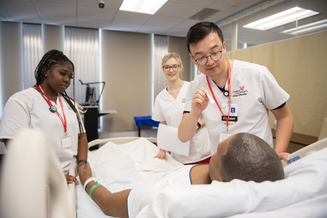 two female nursing students and one male nursing student are seen in clinical setting with a patient laying in the bed