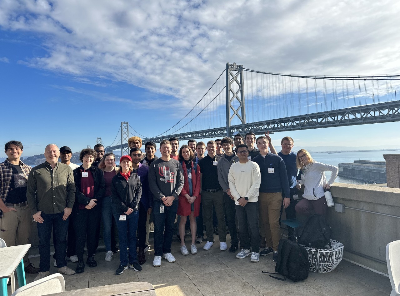 A group of students pose for a photo in front of a bridge.