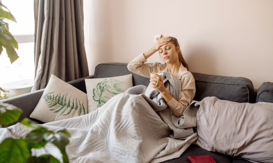 a woman under a blanket while holding her hand to her head