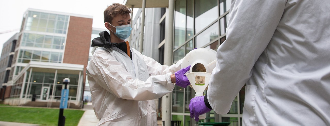Biomedical engineering students in labcoats, masks and gloves collect a sample of wastewater on UC's Uptown campus.