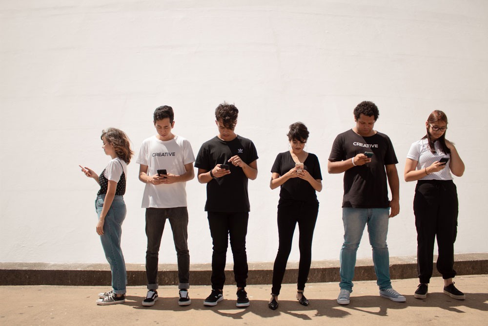 Group of people standing in a line looking down at their smartphones